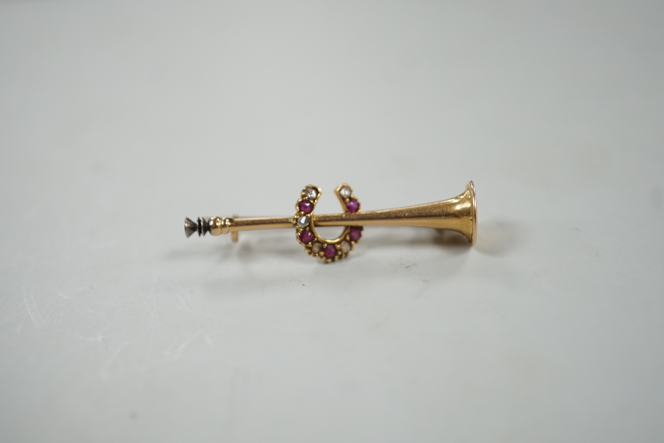 An Edwardian yellow metal, ruby and diamond set hunting horn and horseshoe brooch, 37mm, gross weight 2.6 grams.